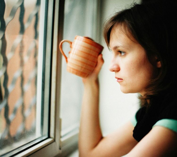 Woman sitting thoughtfully by a window reflecting on unexplained infertility after normal fertility test results
